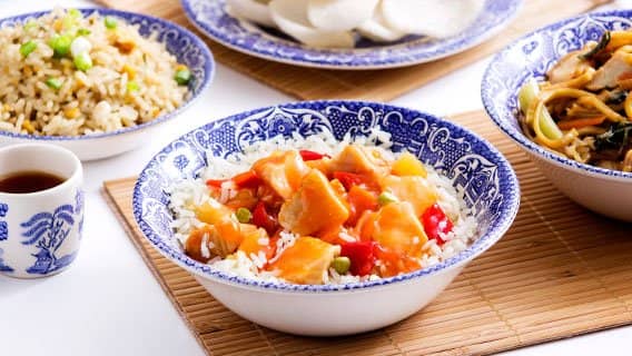 Sweet and sour chicken on rice in a blue-and-white patterned bowl, with egg fried rice and noodles