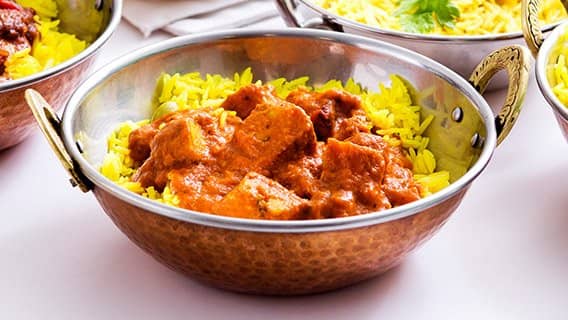 Chicken curry in a copper karahi dish served on yellow pilau rice