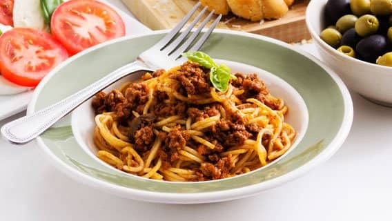 Spaghetti bolognese with fresh basil in a green-rimmed bowl